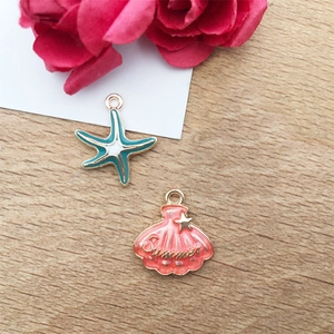 Enamel ocean charms with blue starfish and pink summer shell on a rustic wood background