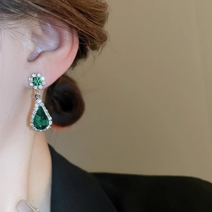Close-up of green teardrop emerald earring with silver crystal setting on a model