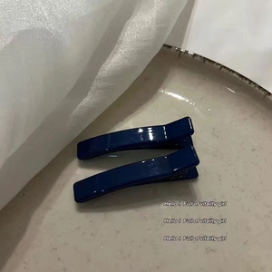 Detail of two dark blue jelly duckbill hair clips on a white ceramic plate background