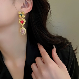 Primer plano de pendientes barrocos con piedras de corazón rojo y dijes de trébol
