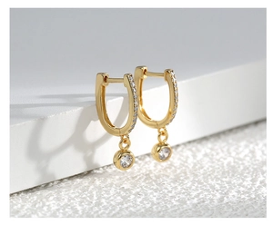 Detailed macro of gold U-shaped earrings with micro-set zircon and round pendant drops