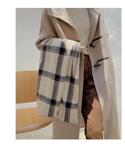 Detail of soft beige cashmere-feel scarf with black and blue plaid pattern held by model