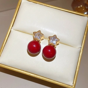 Detailed macro view of gold-plated star earrings with crystals and red pearls in a box