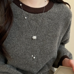 Collier perle en Y argenté avec pendentif flocon sur un pull gris en gros plan
