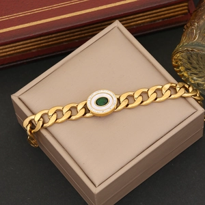 Detailed shot of a gold Cuban link bracelet with a green gemstone on a jewelry box