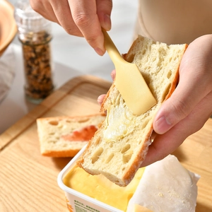 Yellow silicone double-headed jam spatula spreading butter on bread over wooden board