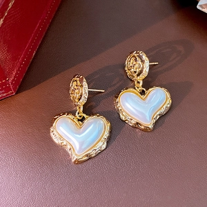 Detail of golden hollow heart earrings with pearlescent stone on brown leather