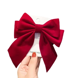 Hand holding a large red velvet bow hair clip for girls against a white background