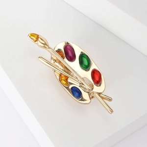 Close-up of golden artist palette brooch with colorful gemstones and paintbrushes