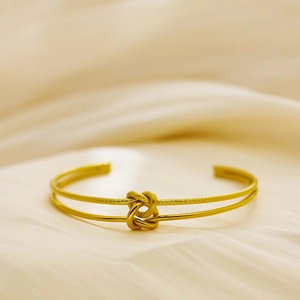 Detail of a double-layered 18k gold-plated C-shaped cuff with sandblasted knot and silk background