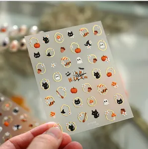 Close-up of Halloween nail stickers with gold outlines of pumpkins, black cats and ghosts
