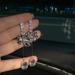 Close-up of silver tassel earrings with a bow design and large square cubic zirconia