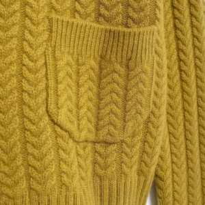 Close-up of mustard yellow cable knit cardigan showing texture details and a pocket design