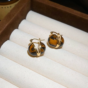Detailed close-up of golden hoop earrings featuring amber resin beads on beige velvet