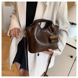 Detail view of brown vintage leather tote bag with a golden chain mini bag charm shown on model