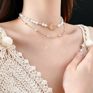 Detail view of double-layered gold necklace with faux pearls and oval gemstone pendant