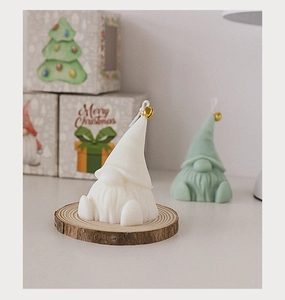 Close-up of white and green Christmas gnome candles with bells on wooden base