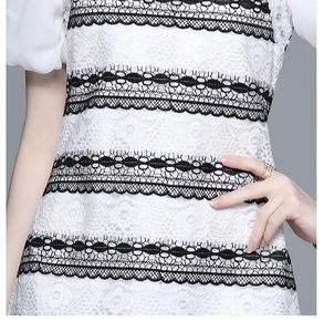 Close-up of white lace dress featuring black wavy trim, pearls, and rhinestone details