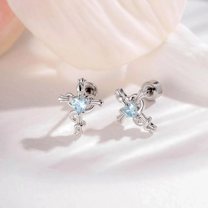 Serpent wrapped cross stud earrings with heart-shaped light blue gemstone on white fabric