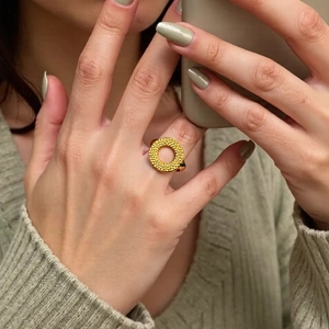 Close-up of golden hollowed ring with hammered texture worn on finger by a model