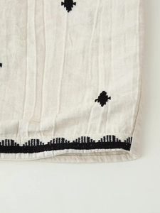 Close-up of beige linen fabric with black geometric embroidery and detailed stitching