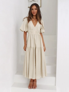 Deep V-neck and puff sleeve details on a beige midi dress worn by a model on steps