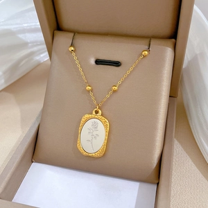 Detailed macro shot of gold rose relief pendant on a minimalist stainless steel necklace