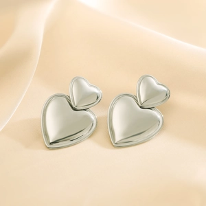 Polished silver double heart earrings displayed on minimalist beige silk fabric backdrop
