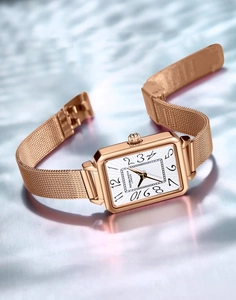 Square rose gold watch with woven mesh strap over elegant rippled water surface
