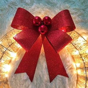 Close-up of glittery red Christmas bow with festive ornaments on a golden wreath