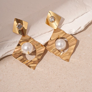 Detail of gold geometric earrings with pearl and rhinestone on white textured stone