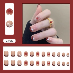 Faux ongles blush rose avec perles et pointes françaises rouges sur mains de mannequin