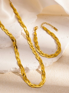 Detailed close-up of braided gold stainless steel necklace and bracelet set on silk