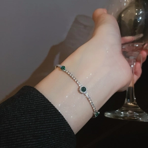 Sparkling silver tennis bracelet with green emerald zircon worn on wrist with glass