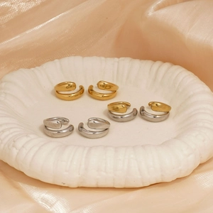 Polished gold and silver C-shaped double ear cuffs set on a white plate and silk background