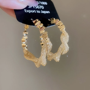 Detailed view of large gold twisted weave hoop earrings with geometric tile texture