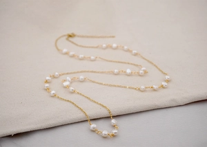 Detailed close-up of a long gold chain necklace featuring small natural freshwater pearls