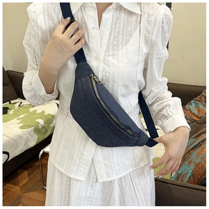 Close-up of a navy denim crescent chest bag with gold zipper shown on a female model
