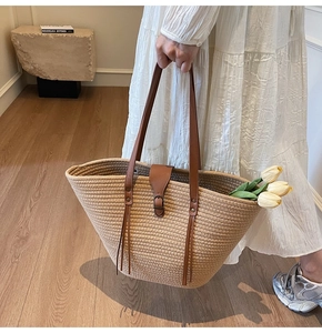 Detail view of woven straw tote bag featuring brown leather straps and buckle closure