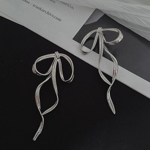 Detail of silver metallic bow earrings with long tassels and polished finish