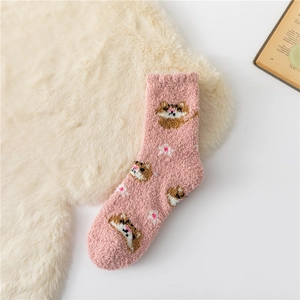 Close-up of pink coral fleece socks featuring cute raccoon and floral patterns on plush rug