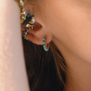 Close-up of golden stainless steel hoop earrings with turquoise stones on a model