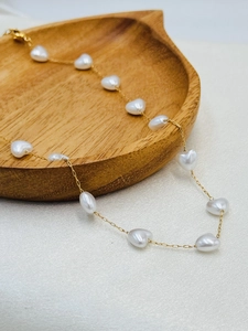 Detail of gold chain necklace featuring white heart-shaped beads on wood tray