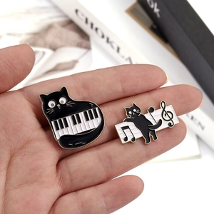Close-up of cute black cat enamel pins with piano and music note designs held in hand