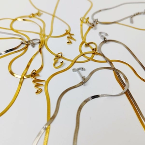 Detailed view of stainless steel flat snake chain necklaces with gold and silver initial pendants.