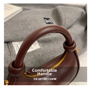 Close-up of the thick cylindrical handle and gold zipper on a dark brown leather crescent bag
