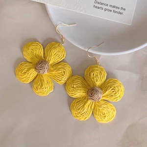 Detail of yellow woven flower earrings with brown centers and gold-colored hooks