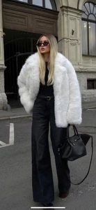 Détail d'un manteau en fausse fourrure blanche avec un pantalon noir large pour l'hiver