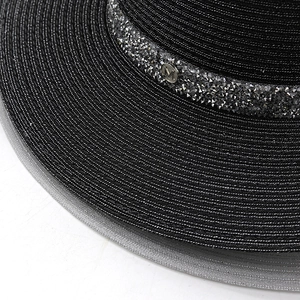 Détail d'un chapeau en paille noir avec bandeau en strass et logo M en métal argenté