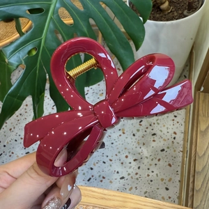 Close-up of a large glossy burgundy bow hair claw clip with golden metal accents